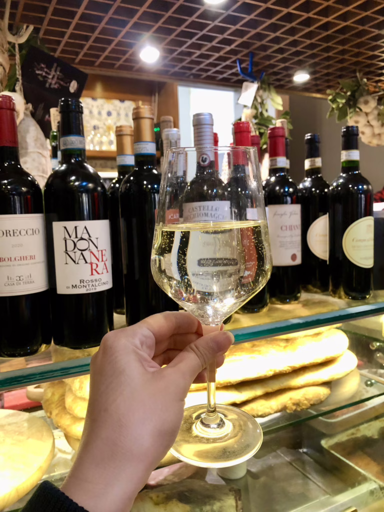 wine glass being held up in front of other bottles of wine in a panini shop in florence italy