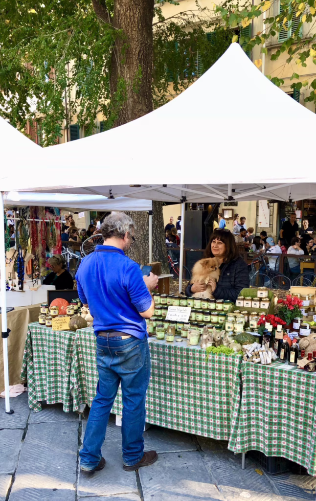 two people at an artisan market stand in piazza santo spirito with a dog. artisans markets are a great way to get offbeat in florence italy
